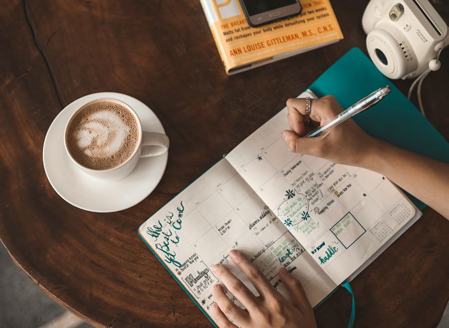 A person writing thoughtfully in a planner beside a warm drink, preparing for the day