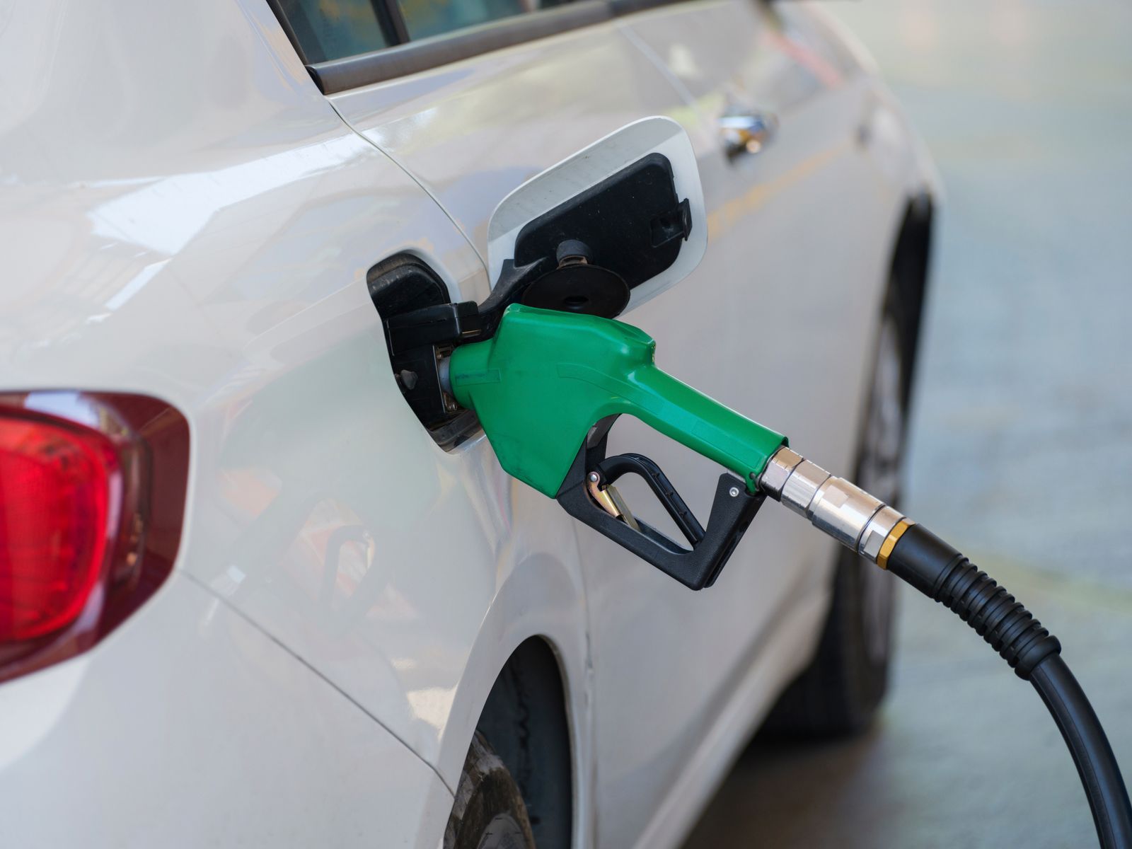 A green fuel nozzle refueling a white car at a gas station
